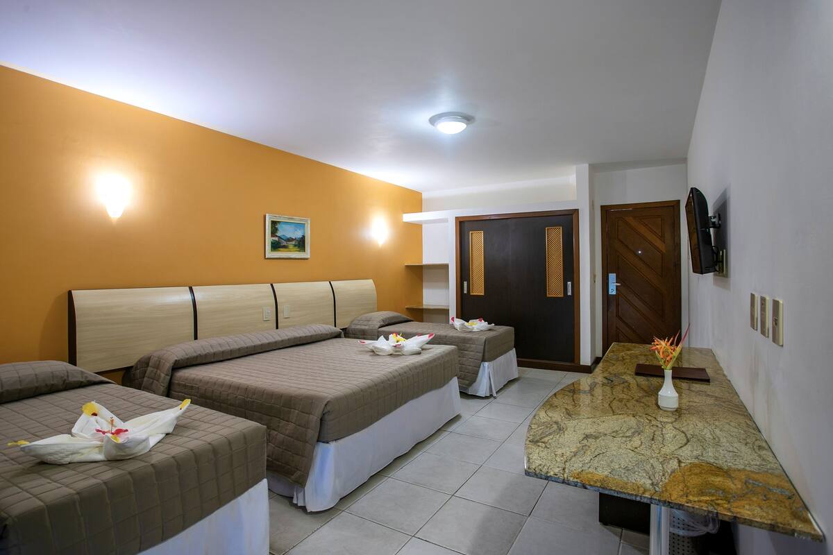 A hotel room with three beds, a marble countertop, a painting on the wall, and a TV mounted on the wall.