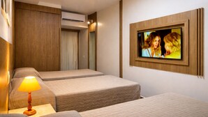 A hotel room with two beds, a wall-mounted TV, an air conditioning unit, and a bedside lamp.