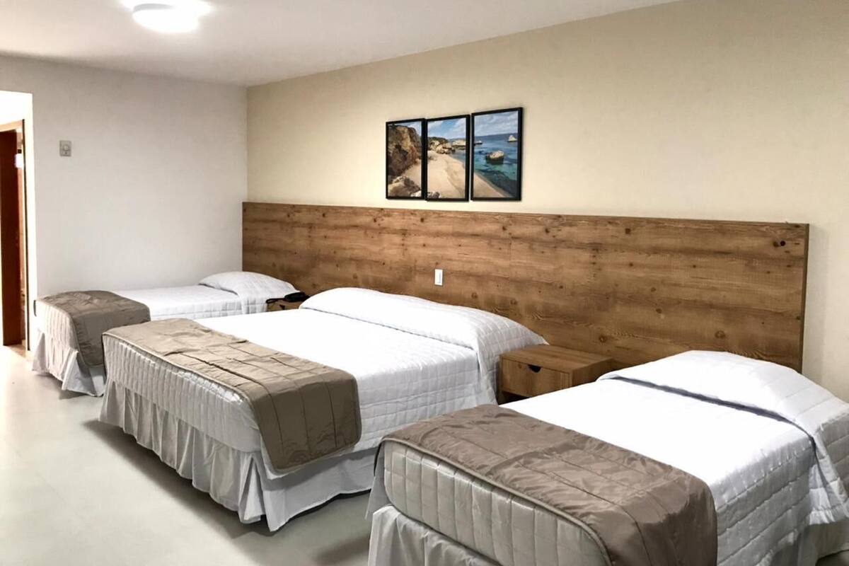 A hotel room with four beds arranged in a row, a wooden headboard, and a wall-mounted picture of a beach scene.