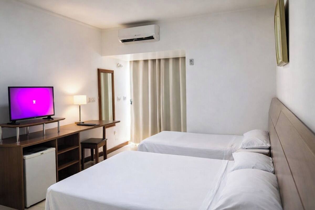A hotel room with two beds, a desk with a computer, a television, and a small refrigerator.