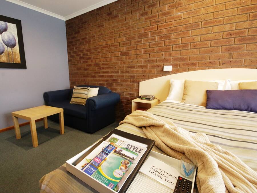 A hotel room with a brick wall, a bed with striped bedding, a blue sofa, a wooden table, and a framed picture on the wall.