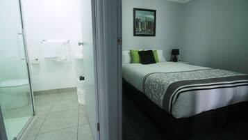 Camera d'albergo con un letto, un comodino, un quadro appeso e un bagno con box doccia in vetro.