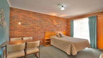 A room with a brick wall, a bed with a striped blanket, a wooden nightstand, a chair, and a table.