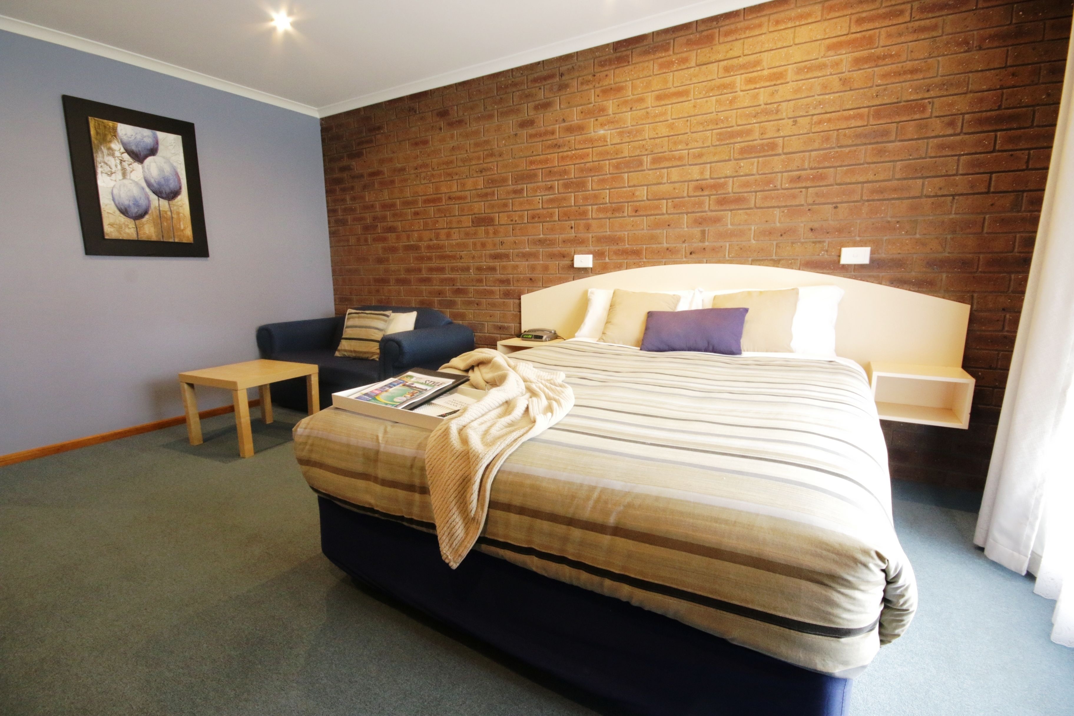 A hotel room with a large bed, a small table, a sofa, and a brick wall.
