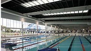 En indendørs swimmingpool med flere baner, et springtårn og et stort område med vinduer.