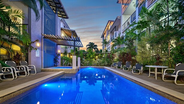 A swimming pool with lounge chairs and tables, surrounded by buildings and greenery. - Getaway On Grafton (Cairns)