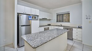 A modern kitchen with white cabinets, stainless steel appliances, and a granite countertop. - Getaway On Grafton (Cairns)