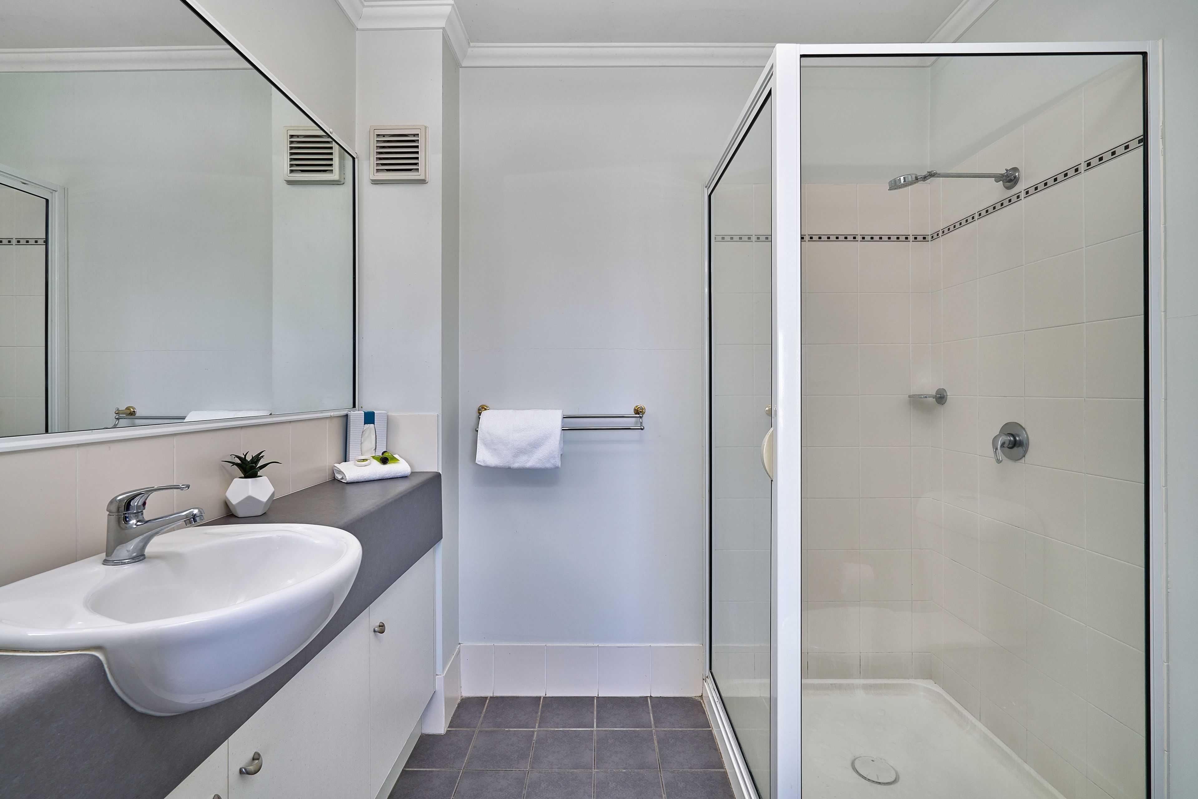 A bathroom with a white sink, a mirror, a towel rack, and a glass-enclosed shower area.