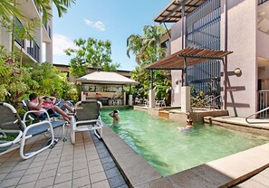 A pool area with lounge chairs, a covered seating area, and a building with a modern architectural style.