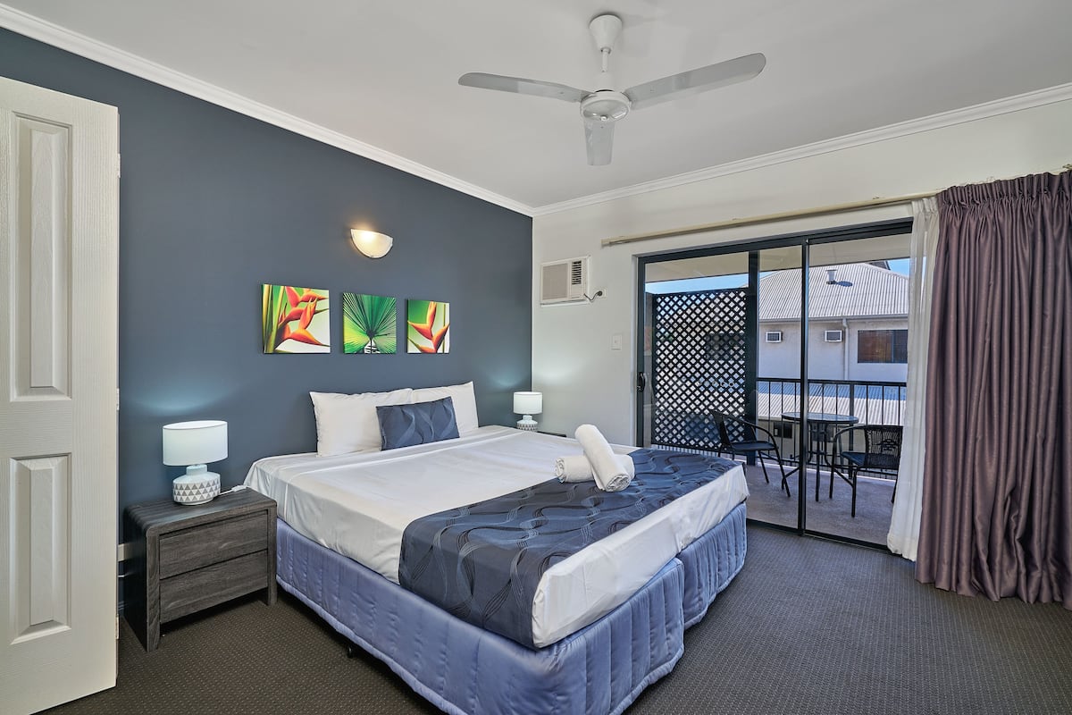 A hotel room with a large bed, two bedside tables, a ceiling fan, and a balcony with a table and chairs.