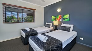 A hotel room with two beds, a ceiling fan, a window with blinds, and artwork on the wall. - Getaway On Grafton (Cairns)