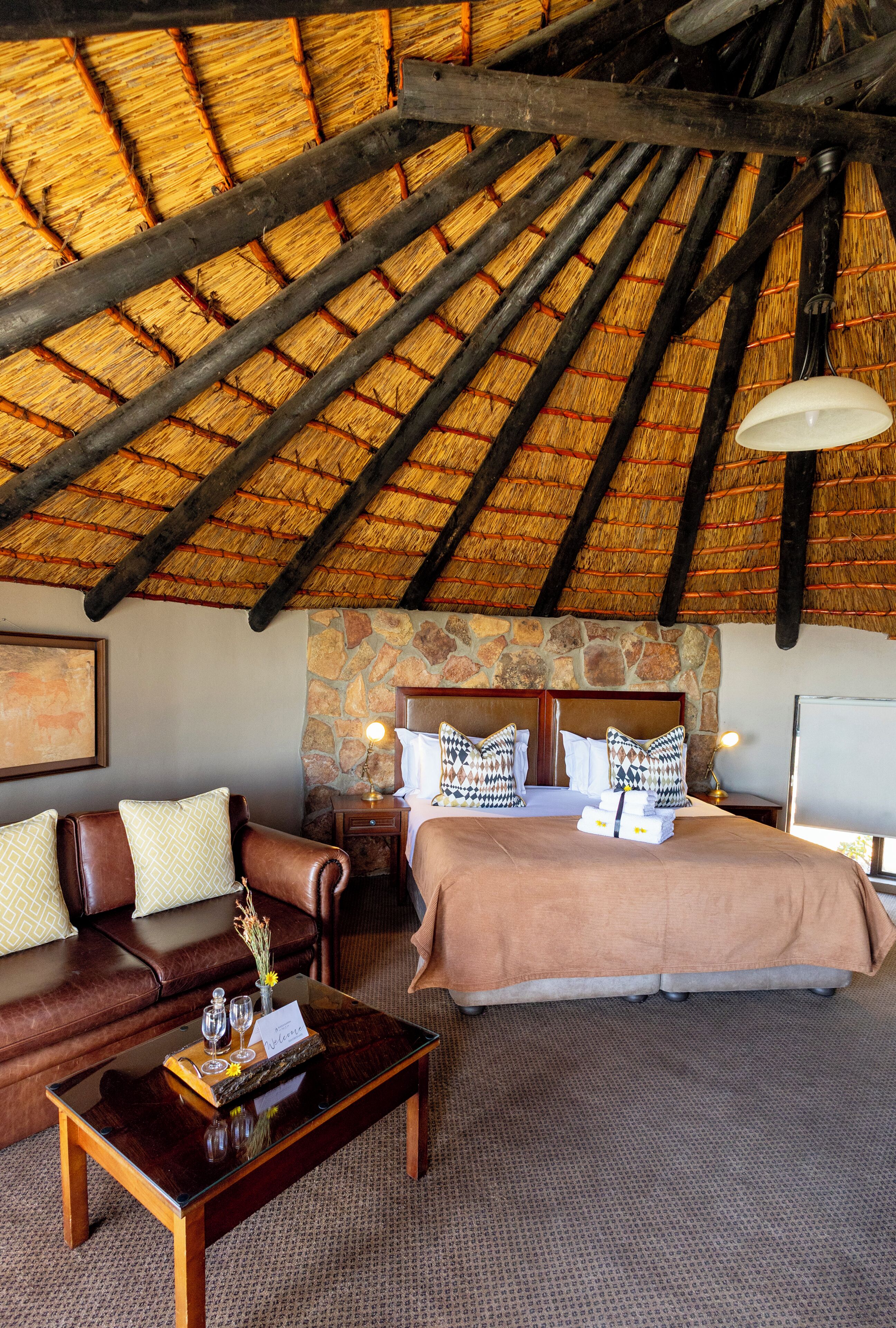 A room with a high ceiling, a stone fireplace, a bed with pillows, a sofa, a coffee table, and a lamp.