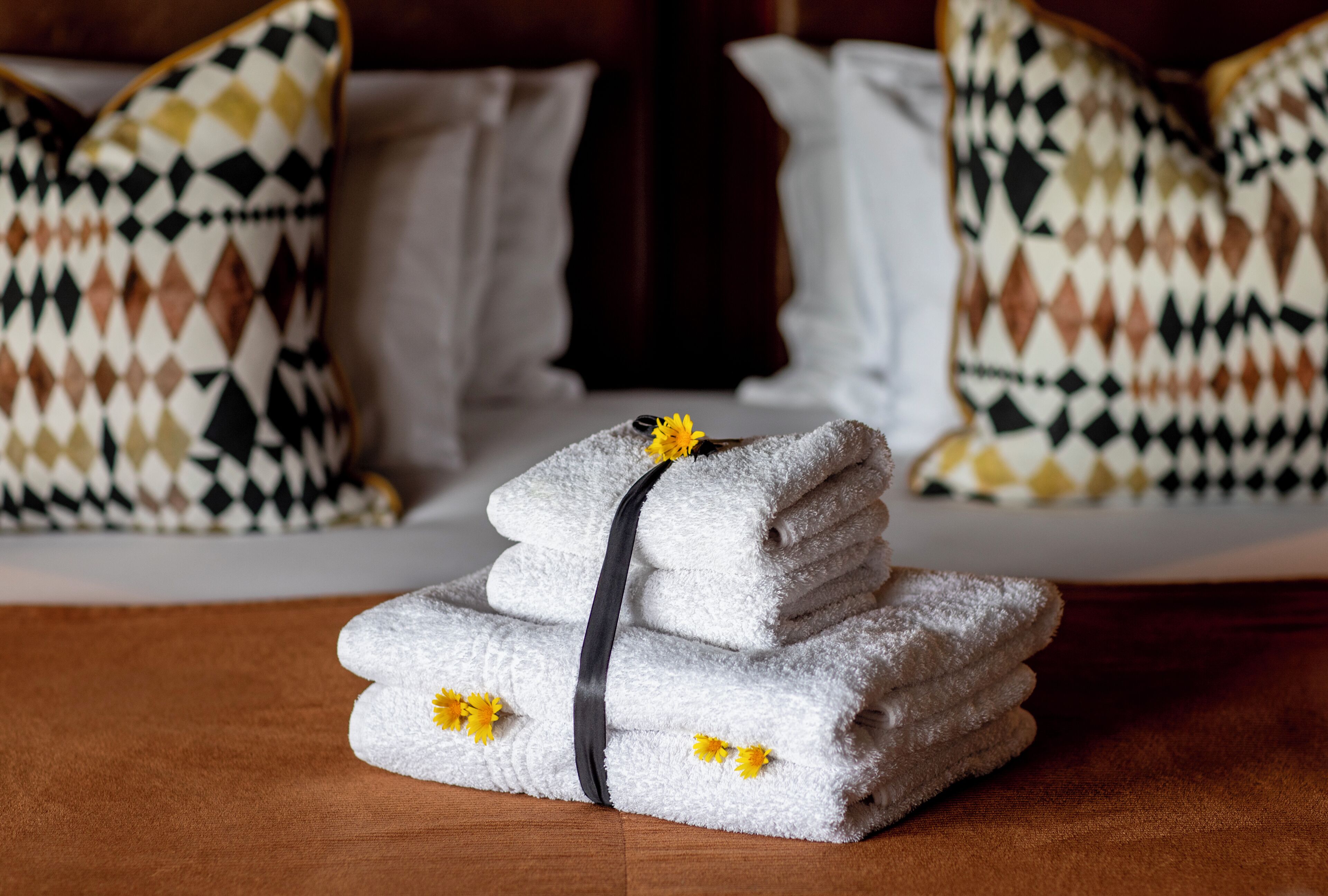 A stack of white towels with a black ribbon and yellow flowers, placed on a wooden surface.