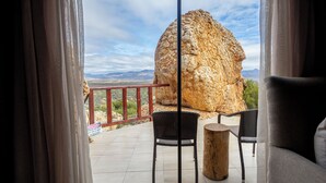 Un balcón con vista a una gran formación rocosa, dos sillas y una mesa de madera.