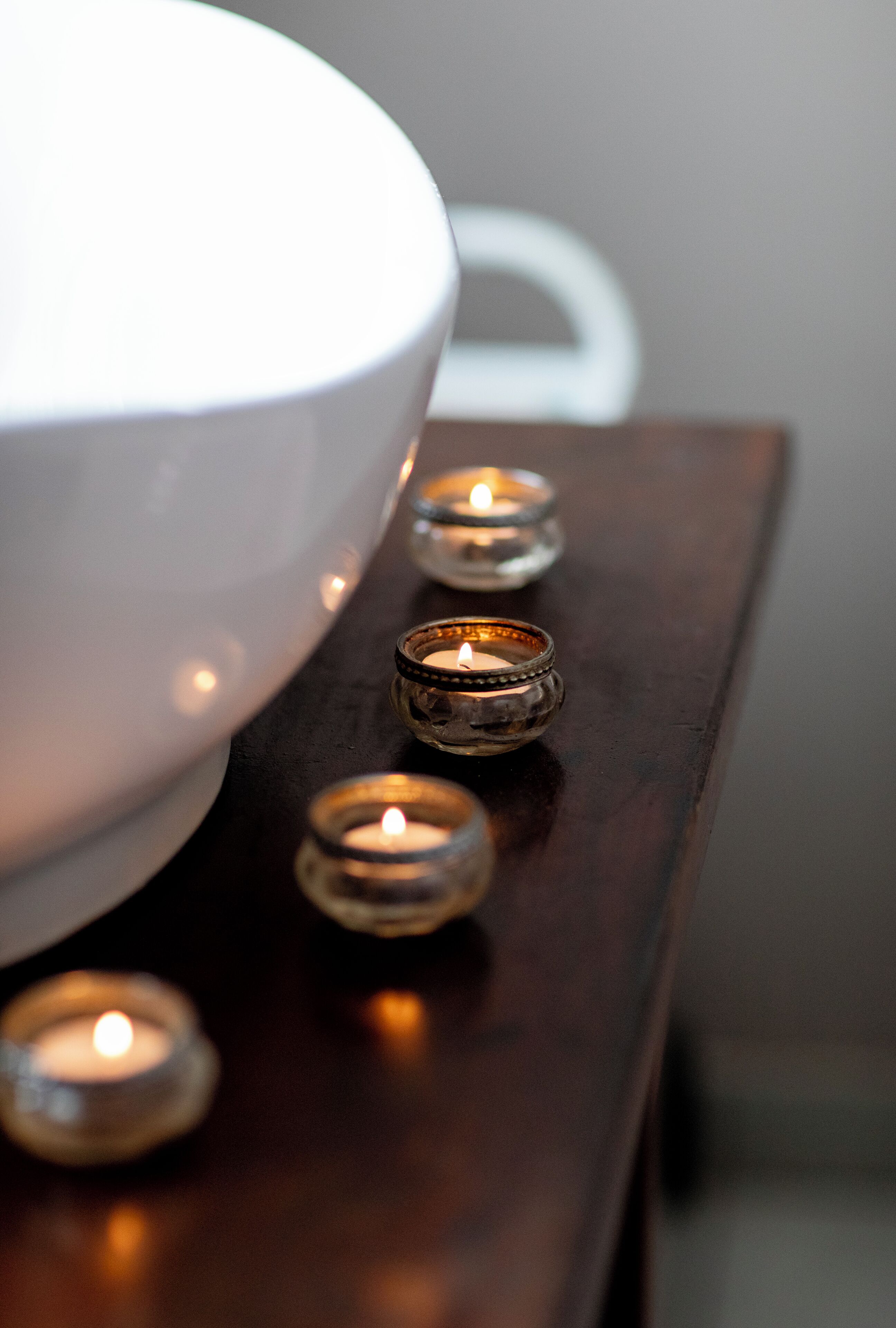 A white bowl on a wooden surface with several lit candles.