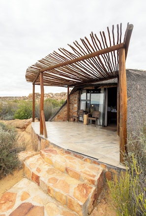 Een terras van stenen leidt naar een houten pergola met uitzicht op een woestijnlandschap.