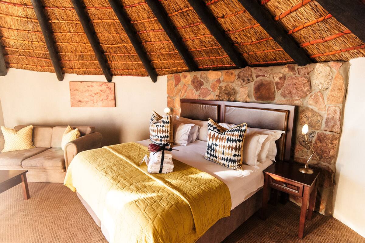 Een hotelkamer met een bed, een bank, een nachtkastje en een stenen muur.