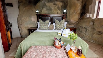 Un dormitorio con una cama grande, dos mesitas de noche, un cabecero de madera y una pared de piedra.