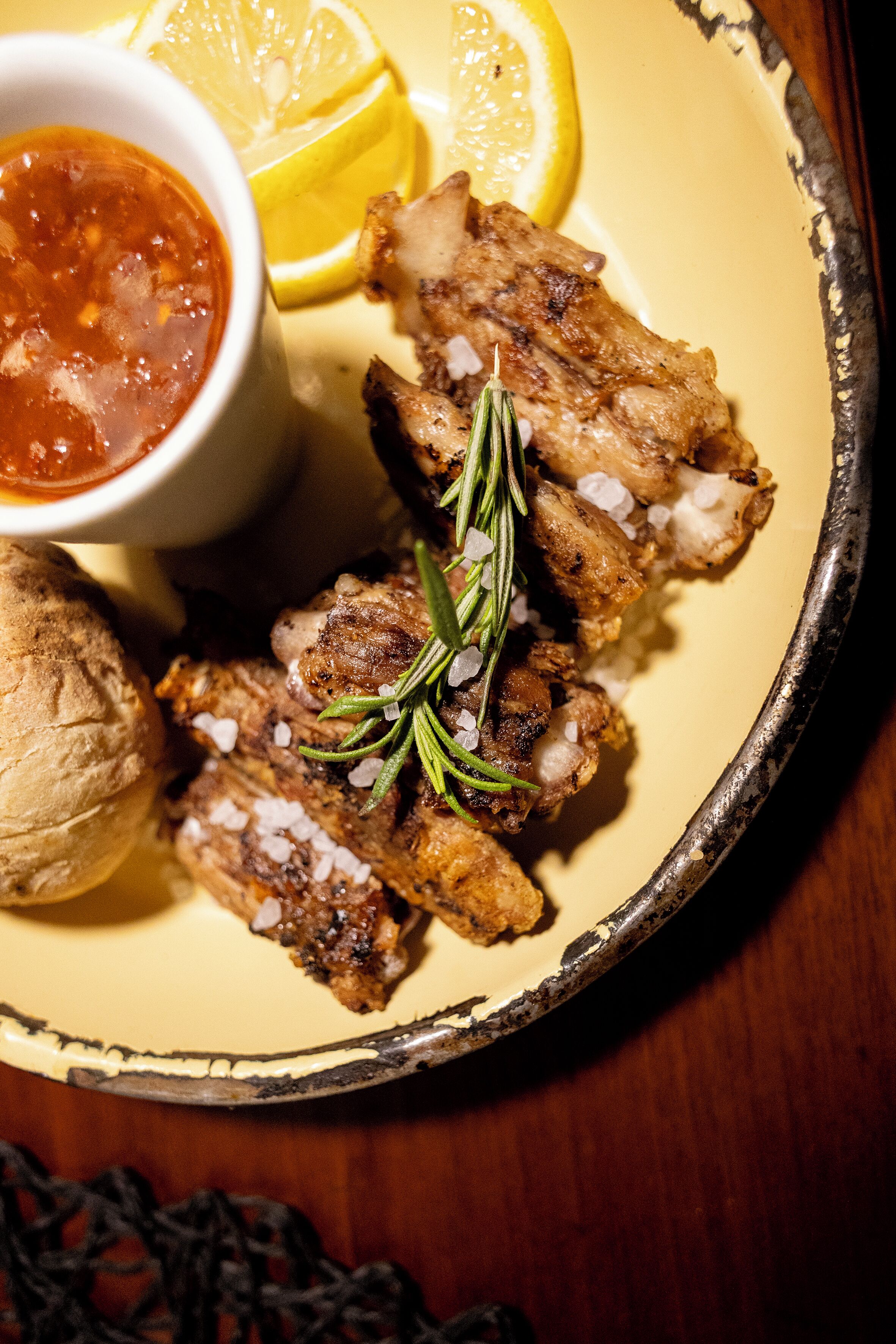 A plate with grilled meat, lemon slices, and a small bowl of sauce.
