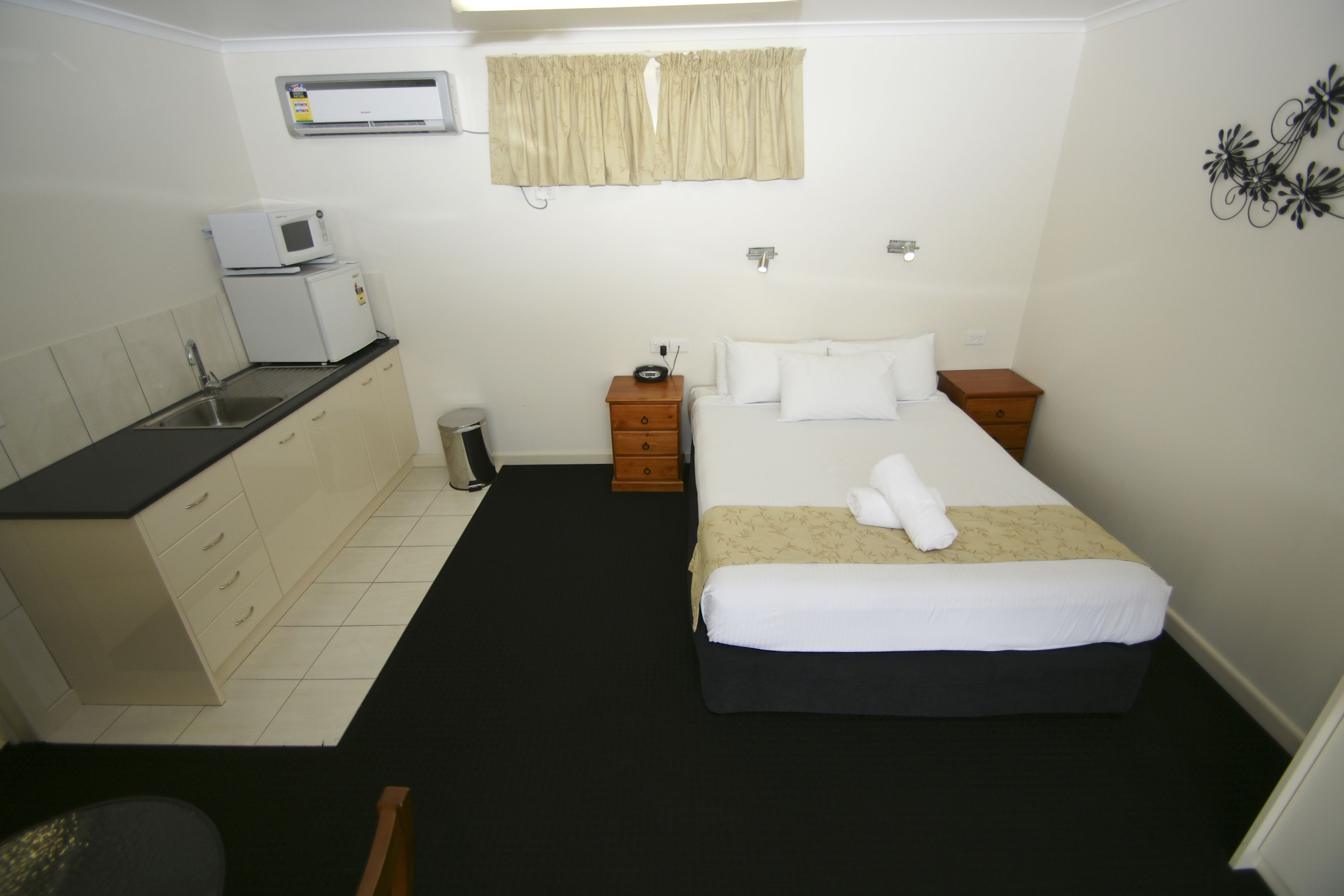 Habitación de hotel con cama, mesita de noche, microondas, lavamanos y ventana con cortinas.