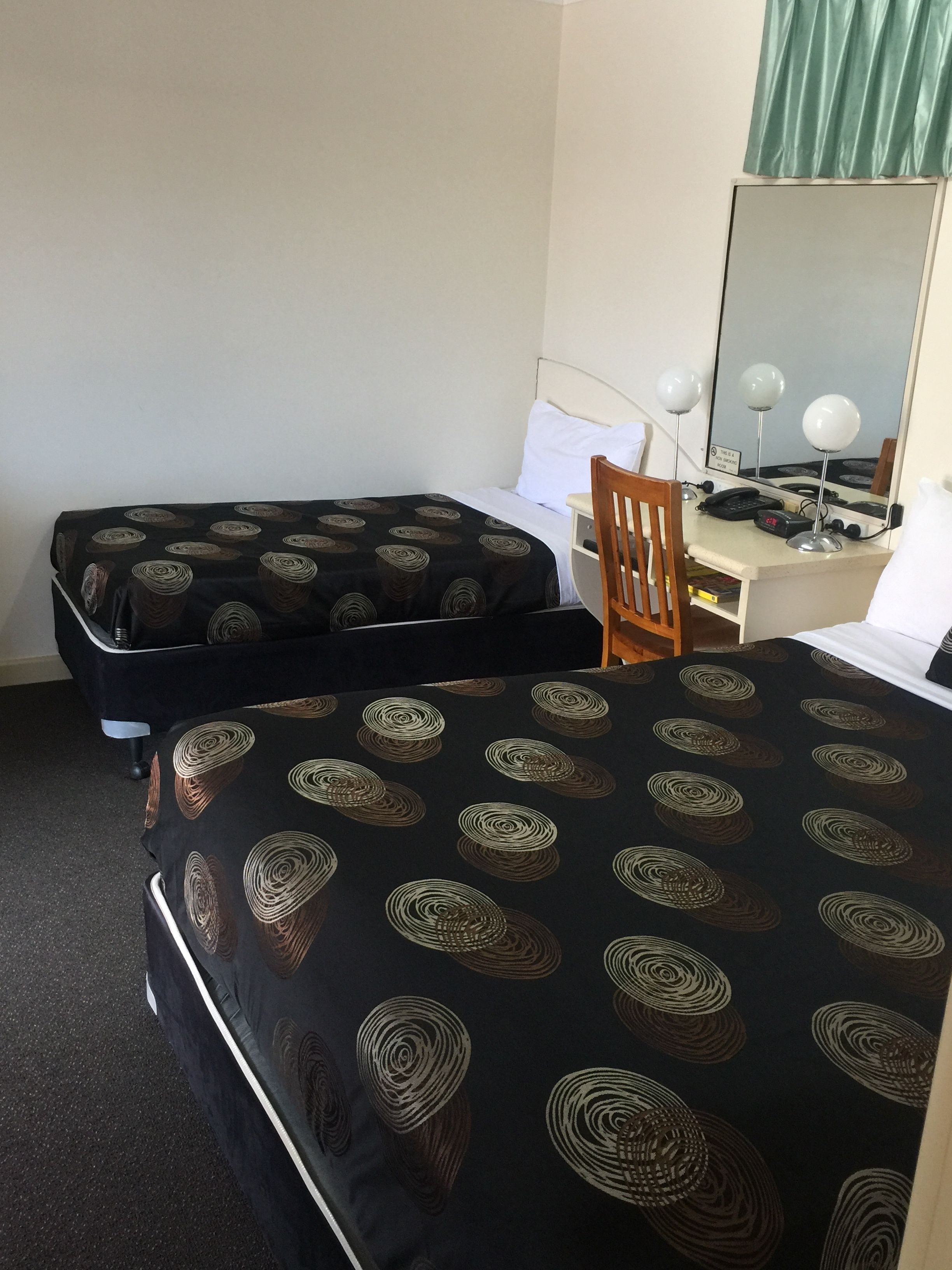A hotel room with two beds, a desk with a chair, a telephone, and a mirror.