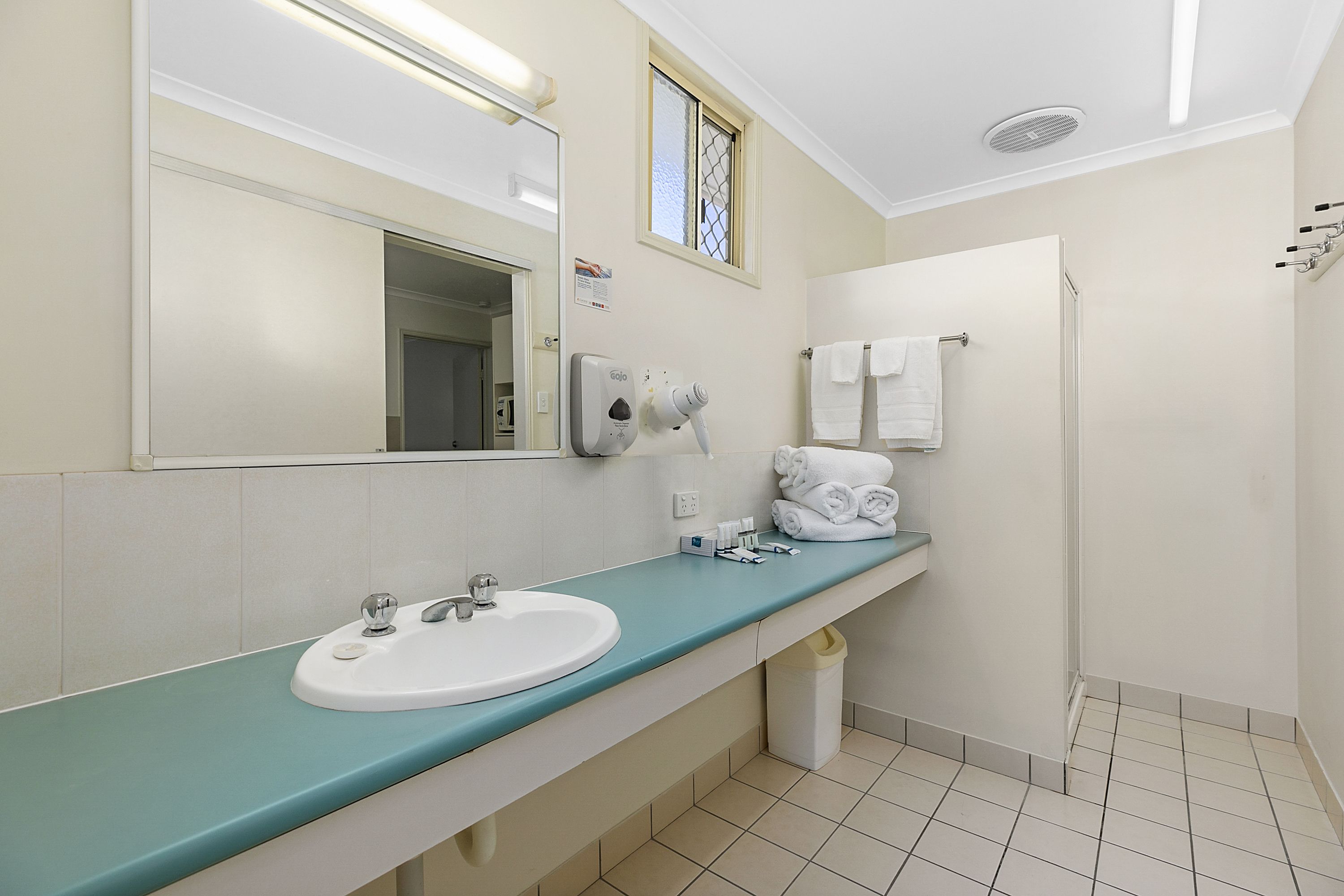 Un baño con lavamanos, espejo, toallero y ventana.