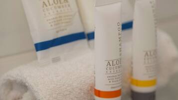 Un baño con repisa de vidrio que contiene artículos de tocador, incluyendo una toalla blanca y dos botellas de champú.