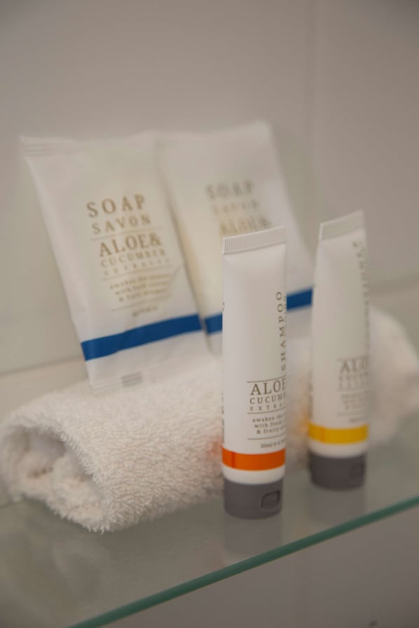 Un baño con repisa de vidrio que contiene artículos de tocador, incluyendo una toalla blanca y dos botellas de champú.