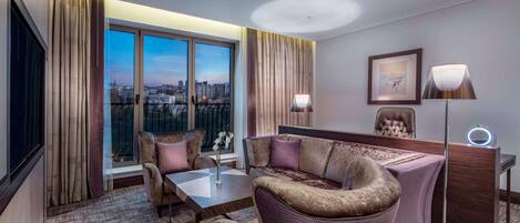Un hotel moderno con una ventana grande que ofrece vista a la ciudad, un conjunto de sofás, un escritorio con lámpara y un cuadro en la pared.