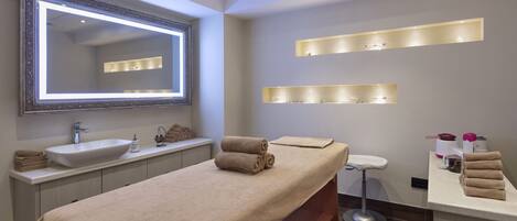 A modern bathroom with a large mirror, a sink, a massage table, and shelves with toiletries.