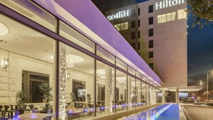 A modern hotel exterior with a long, illuminated water feature in front.