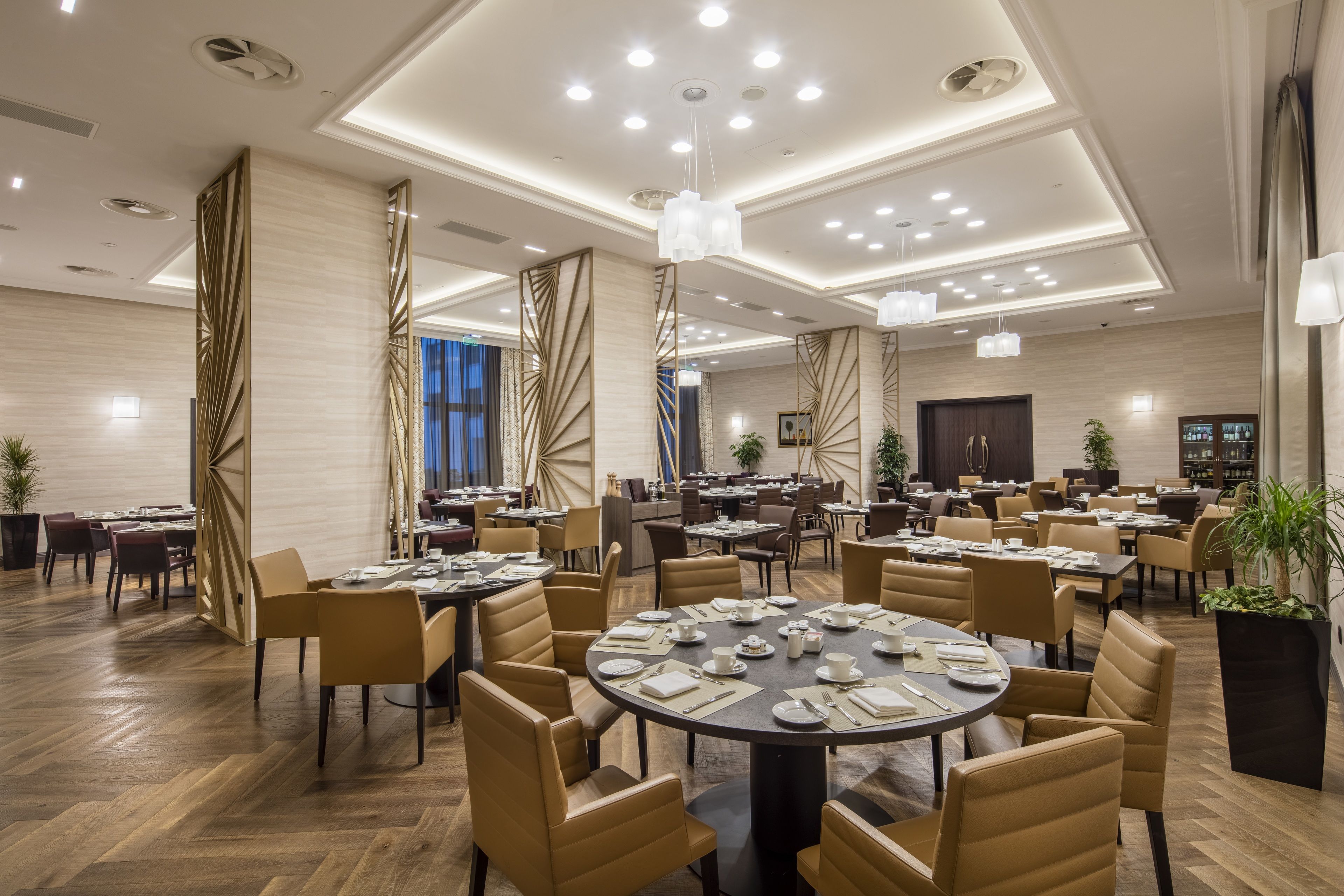 A spacious hotel dining area with multiple round tables set for dining, surrounded by comfortable chairs.