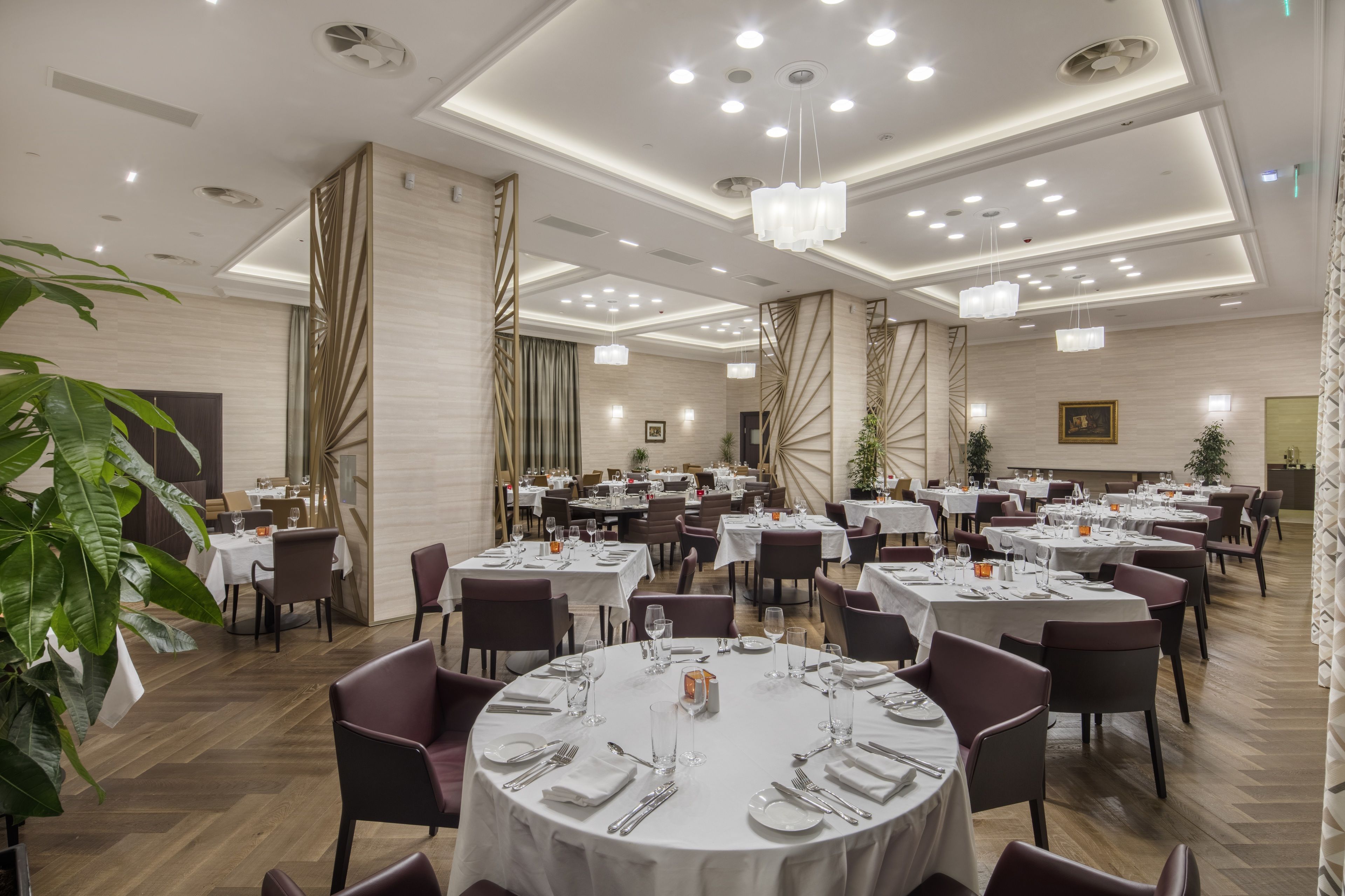A spacious dining area with round tables, chairs, and a modern ceiling design.