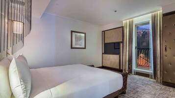 Hotelkamer met een groot bed, een ingelijst schilderij aan de muur en uitzicht op een stadsgezicht door een open deur.