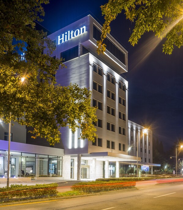 A modern hotel with a prominent "Hilton" sign, a glass entrance, and a well-lit facade. - Hilton Podgorica Crna Gora (Podgorica)