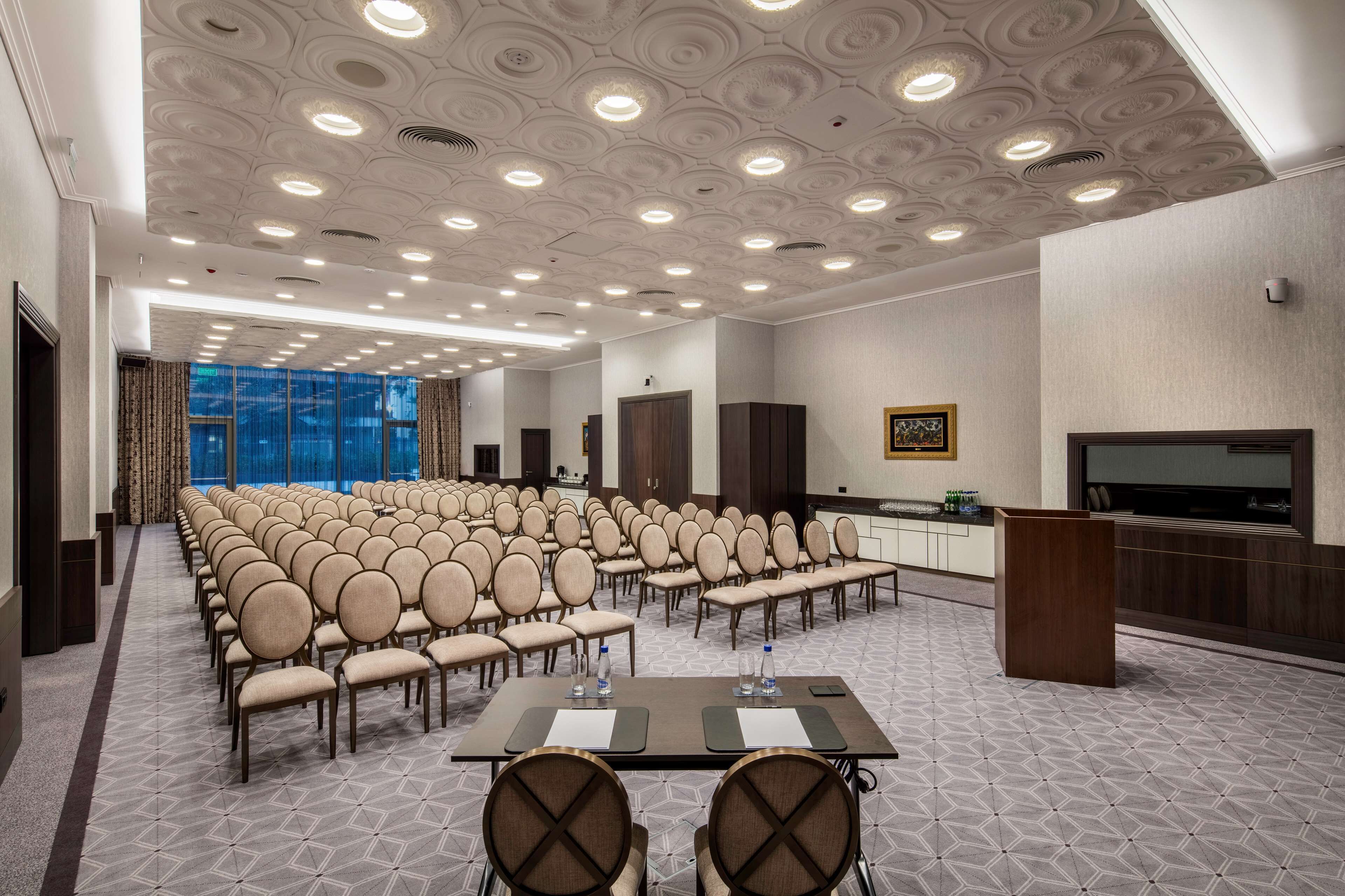A conference room with rows of chairs, a long table with water bottles, and a large screen.