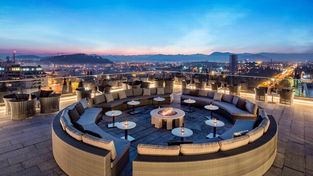 A rooftop lounge with a circular seating area, multiple tables, and a fire pit.