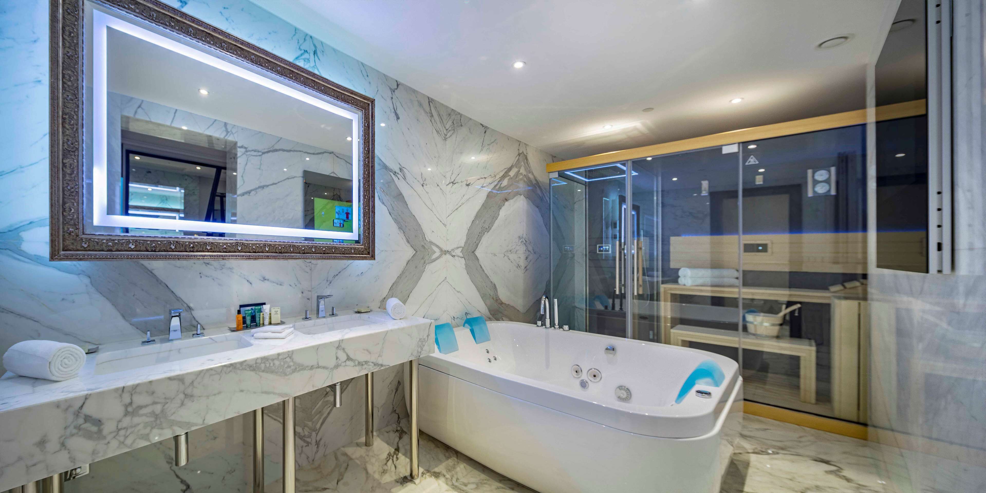 A modern bathroom with a marble vanity, a freestanding bathtub, and a glass shower enclosure.