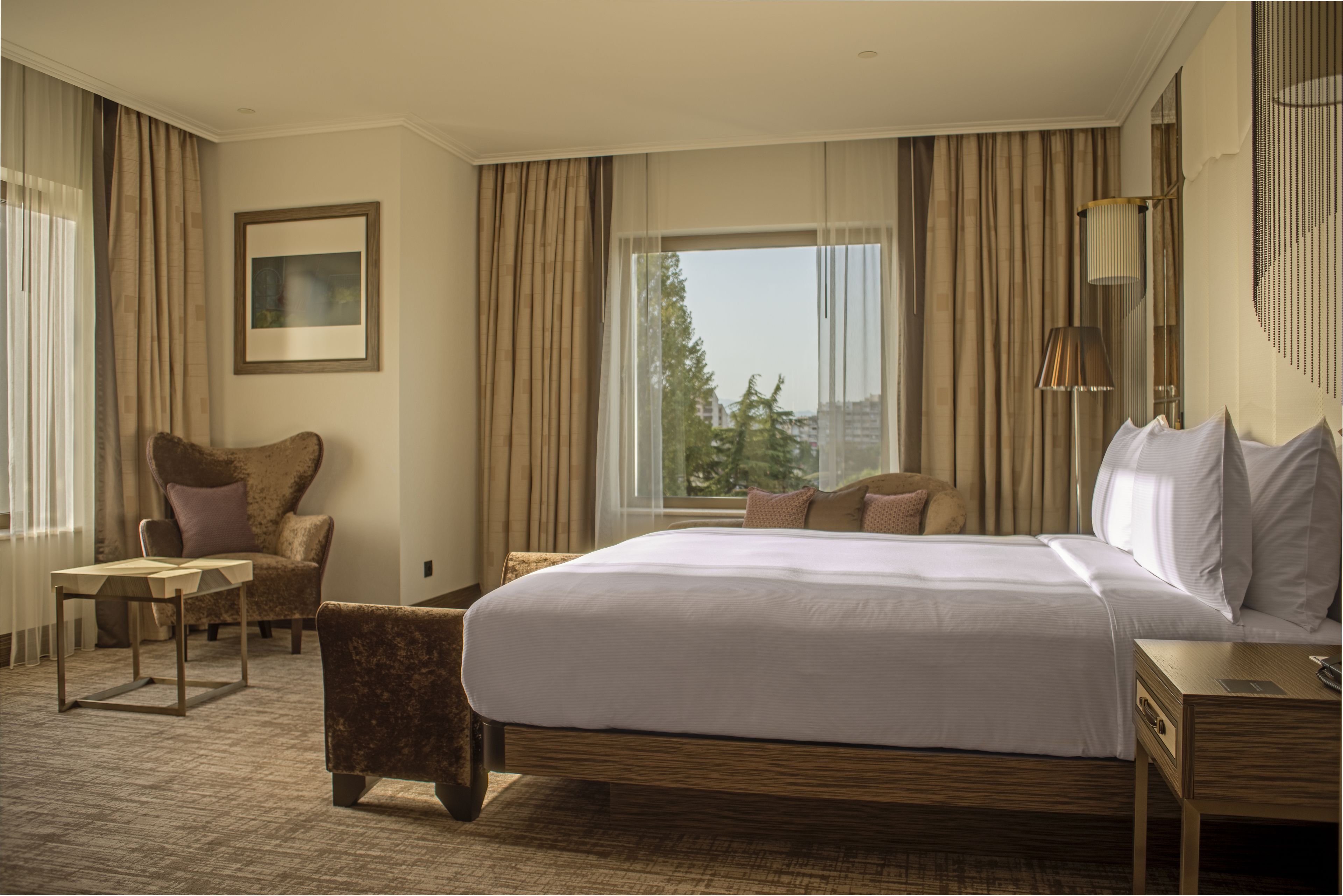 A hotel room with a large bed, a chair, a table, and a window with curtains.