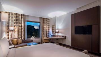 Una habitación de hotel con una cama grande, un escritorio con lámpara, una silla y un televisor montado en la pared.