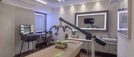 Um spa moderno com mesa de massagem, toucador com espelho e iluminação, e televisão na parede.