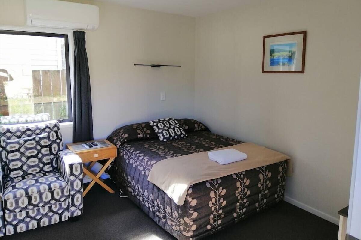 A small room with a bed, a chair, a table, and a window.