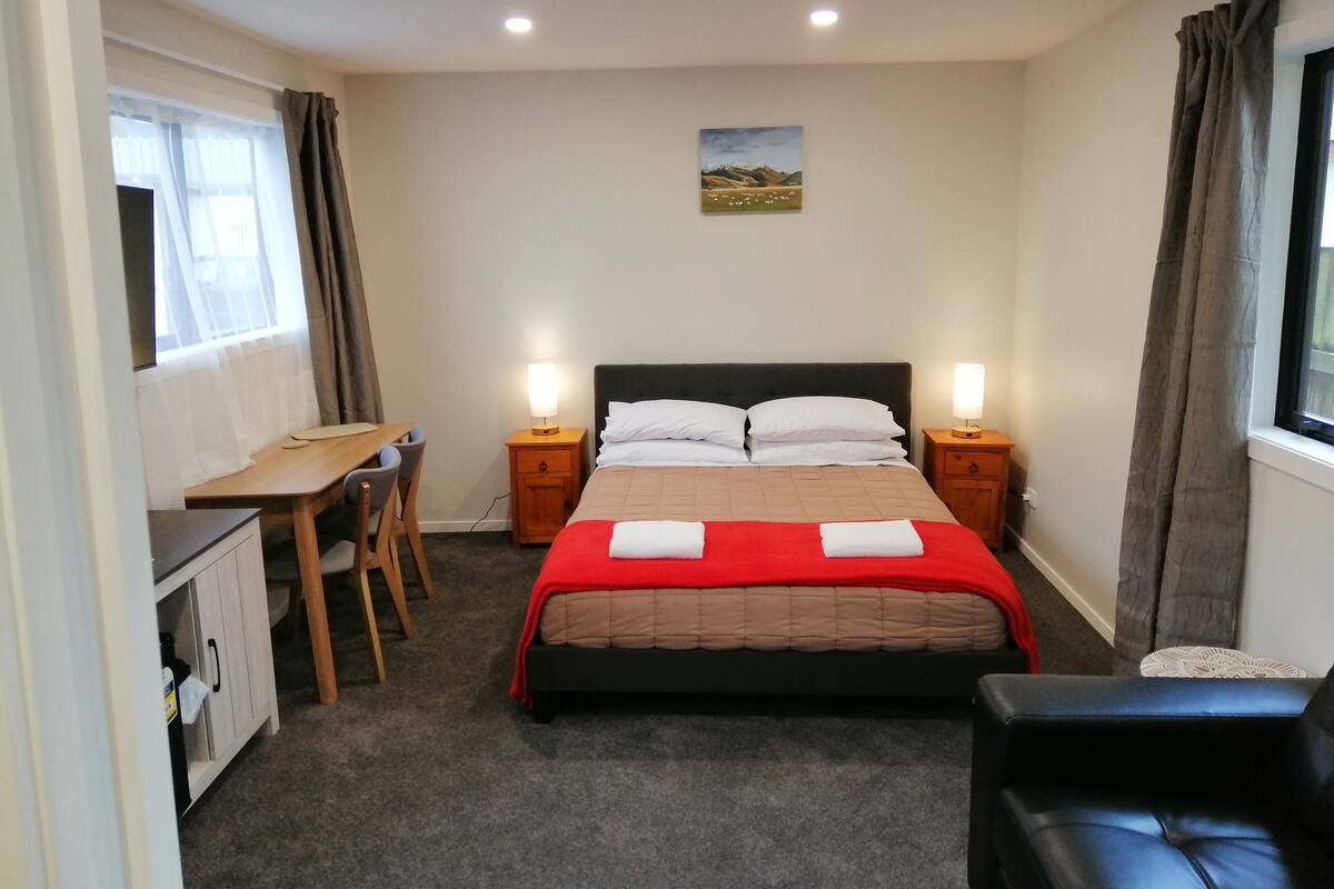 A bedroom with a bed, bedside tables, a desk, and a chair.