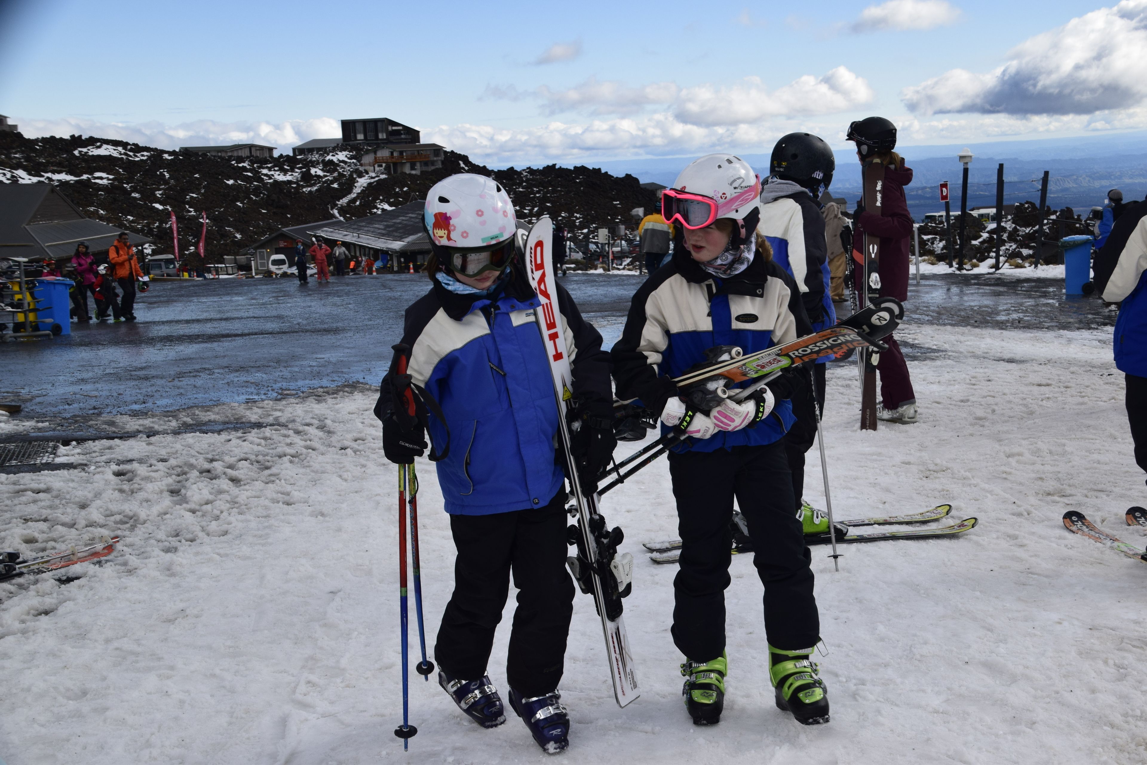 A snowy outdoor area with people holding skis and poles, likely a ski resort.