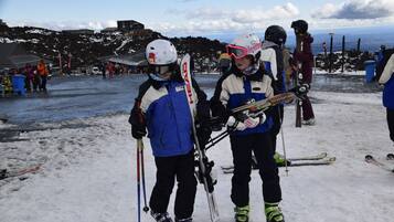 A snowy outdoor area with people holding skis and poles, likely a ski resort.