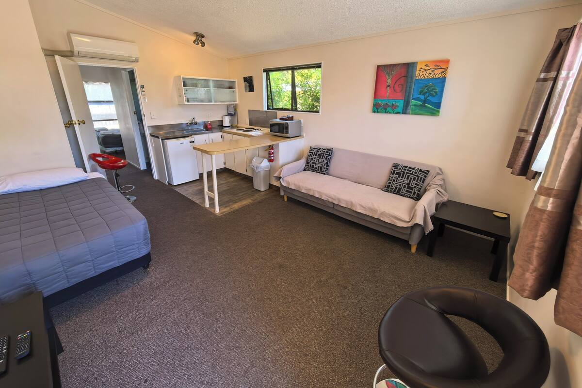 A compact room with a kitchenette, a sofa, a bed, and a small table.