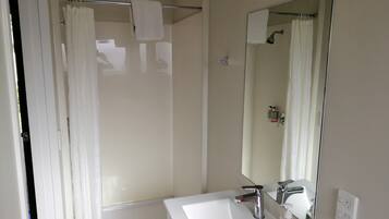 Un baño con lavamanos blanco, un espejo, cortina de ducha y toallero.
