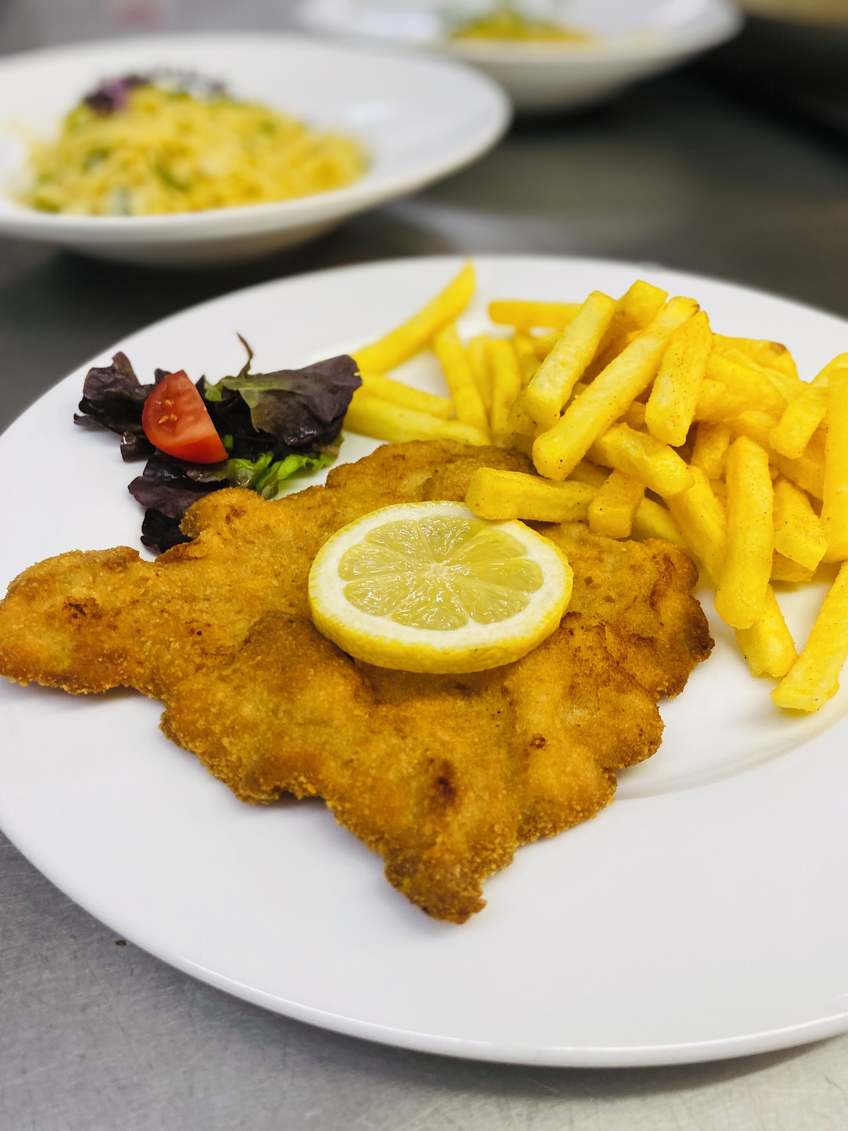 Un plato con una milanesa, una rodaja de limón y papas fritas.