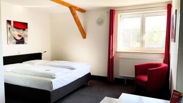 Une chambre à coucher avec un lit, une chaise rouge, une table et une fenêtre avec des rideaux.