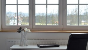 A desk with a laptop, a vase with flowers, and a window with a view of trees and buildings. - Landhotel Zerlaut (Kisslegg)